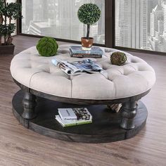 a round coffee table with magazines on it in front of a window and potted plant