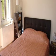 a bed sitting next to a window with a lamp on it's headboard