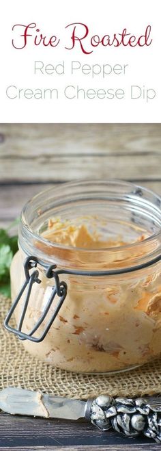 a glass jar filled with red pepper cream cheese dip on top of a wooden table