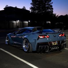 a blue sports car parked in a parking lot at night with its lights turned on