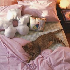 a cat laying on top of a bed next to pillows and stuffed animal toys in a bedroom