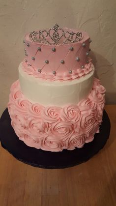 a three tiered cake with pink frosting roses and a tiara on top