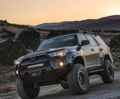 the toyota 4runner is driving on a dirt road with mountains in the background at sunset