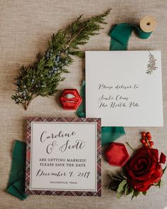 the wedding stationery is laid out with red roses, greenery and rings on it