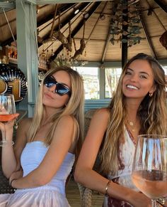 two beautiful women sitting next to each other holding wine glasses