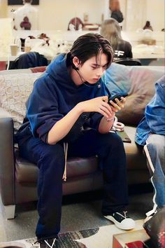 a boy sitting on a couch looking at his cell phone while listening to headphones