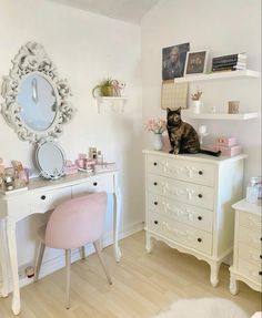 a cat sitting on top of a white dresser next to a mirror and pink chair