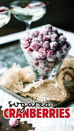 a glass bowl filled with sugared cranberries on top of a table next to two wine glasses