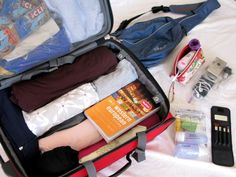 an open suitcase filled with clothes and other items on top of a white sheet covered bed