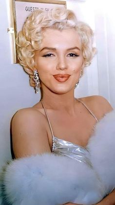 a woman with blonde hair wearing a silver dress and fur stole around her shoulders, posing for the camera