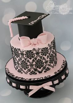 a pink and black cake with a graduation cap on top, decorated with lace and ribbon