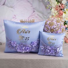 two blue pillows with crowns on them sitting next to each other in front of flowers