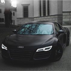 a black sports car parked in front of a white building with the sun behind it