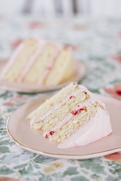 two slices of cake on plates sitting on a floral tableclothed table cloth, one slice is white and the other has pink frosting