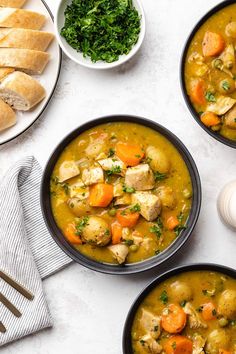 three bowls filled with chicken and vegetable soup next to bread, parmesan croutons