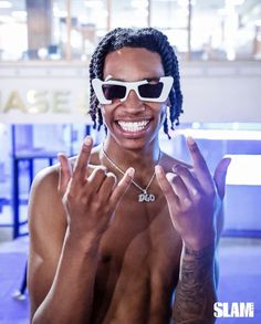 a shirtless man wearing white sunglasses making the peace sign with his hands and smiling