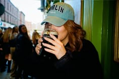 a woman drinking from a beer glass while wearing a green hat