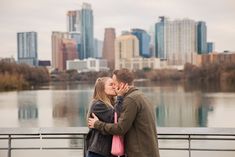 a man and woman kissing in front of a body of water with buildings in the background