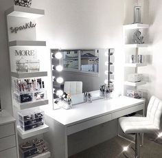 a white desk topped with lots of drawers under a mirror and lighted lights above it