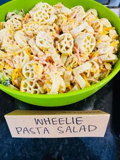 a green bowl filled with pasta salad next to a sign