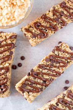 granola bars with chocolate drizzled on them next to a bowl of cereal