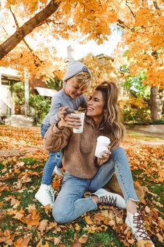 a woman and child sitting on the ground with leaves in front of them holding coffee cups