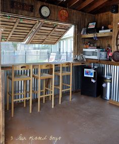 a kitchen area with several stools and a bar in the center, under a roof made out of shipping containers