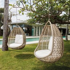 two hanging chairs in front of a swimming pool with trees and grass around them,