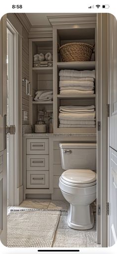 a white toilet sitting inside of a bathroom next to a closet filled with folded towels