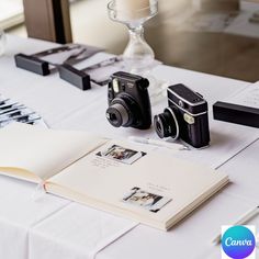 two cameras sitting on top of a white table next to an open book and pen