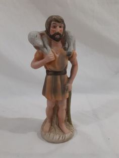 a figurine of jesus holding a cat on his shoulder and standing in front of a white background