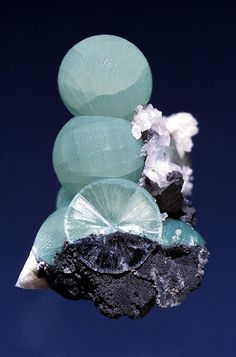 a cluster of green and black rocks on top of each other in the blue sky