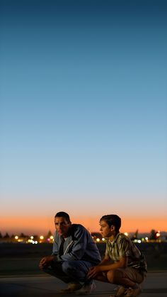 two men sitting on the ground at dusk