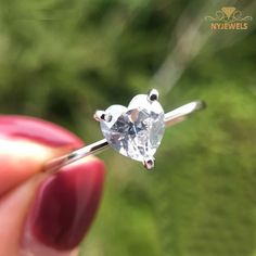 a person holding a ring with a diamond on the top and bottom, in front of some trees