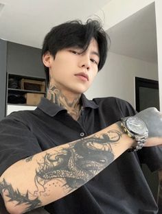 a man with tattoos on his arm holding onto a wrist watch and looking at the camera