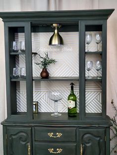 a green china cabinet with wine glasses on top and a bottle in the bottom shelf