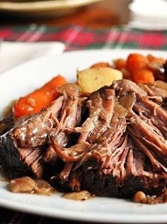 a white plate topped with roast beef and carrots on top of a wooden table