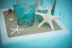 two starfishs are sitting on the sand next to glasses