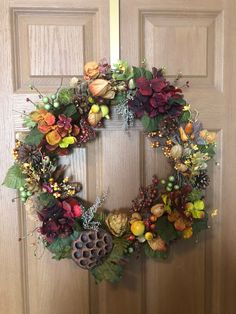 a wreath on the front door with flowers and pine cones hanging from it's sides