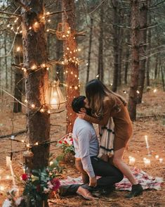 a couple kissing in the woods surrounded by candles and flowers, with lights strung all around them