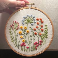 a hand holding a hoop with flowers on it and the embroidery is done in different colors