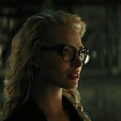 a woman wearing glasses looking off to the side in a dimly lit room with dark lighting