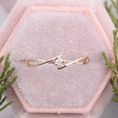 a diamond ring sitting on top of a pink velvet box next to some green plants