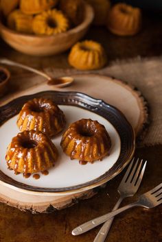 three donuts sitting on a plate with forks and spoons next to some pumpkins