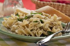 a green plate topped with pasta and spinach covered in sauce next to a slice of bread