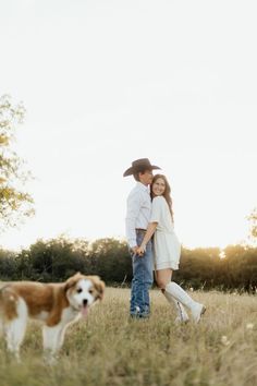 a man and woman are standing in the grass with their dog