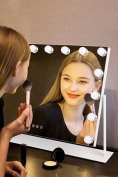 a woman is looking at her face in front of a mirror with lights on it