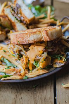 a sandwich and french fries on a plate with cheese sauce in the middle, sitting on a wooden table