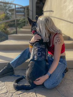 a woman sitting on the ground with her dog and holding it up to her face