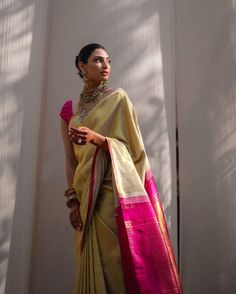 a woman in a yellow and pink sari standing next to a white wall with her hand on her hip